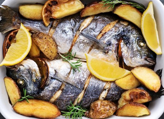 Baked gilt-head bream (dorade) fish with potatoes, herbs and spices.