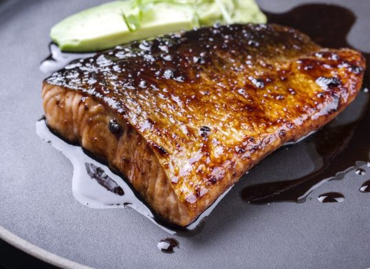 Minimalistic design Japanese salmon fish filet with avocado and wasabi creme glazed in teriyaki sauce as closeup on a modern design plate