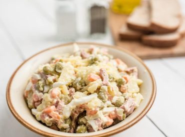 Bowl of traditional Russian salad called Olivie, Russian New Year or Christmas salad on wooden background. Salad from cooked vegetables. Potato salad.