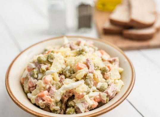 Bowl of traditional Russian salad called Olivie, Russian New Year or Christmas salad on wooden background. Salad from cooked vegetables. Potato salad.