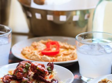 Ouzo in short glasses with ice. Appetizers of seafood in plates. Blur backdrop, close up, details