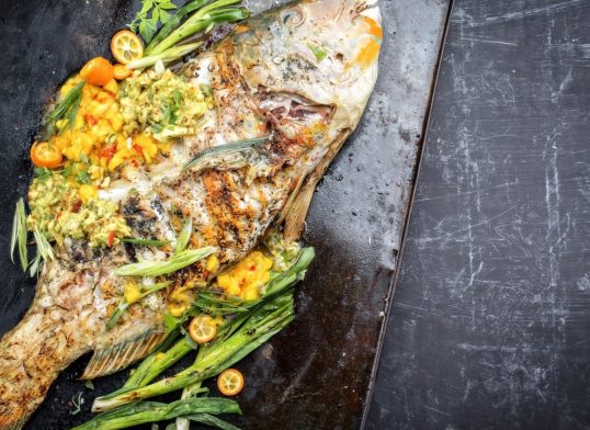 Traditional BBQ parrotfish with mango salsa as top view on a black board copy space right
