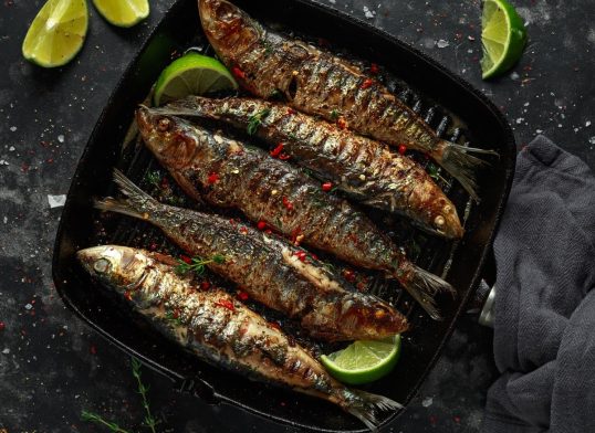 Grilled sardines with thyme, chili and lime wedges on cast iron skillet