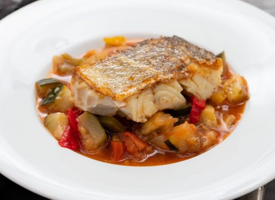 cod fish with vegetables in white plate on ceramic background