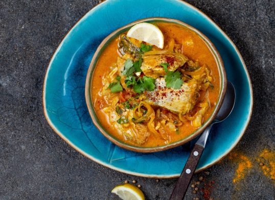INDIAN FOOD. Traditional KERALA FISH CURRY with naan bread, gray plate, black background