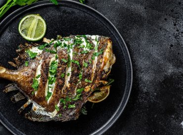 Grilled John Dory fish with lime and parsley in a pan. Black background. Top view. Copy space