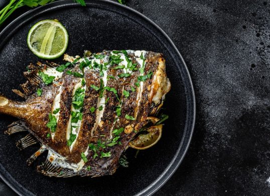 Grilled John Dory fish with lime and parsley in a pan. Black background. Top view. Copy space