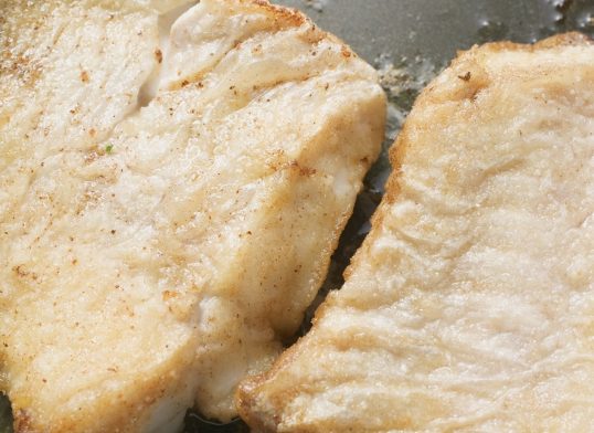 Two fried fish fillets in frying pan (close-up)