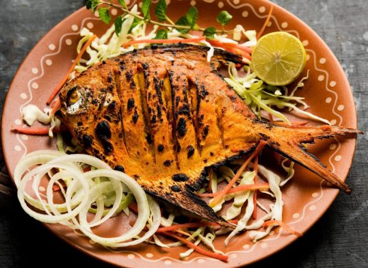 Tandoori Pomfret fish cooked in a clay oven and garnished with lemon , mint, cabbage and carrot salad. Selective focus