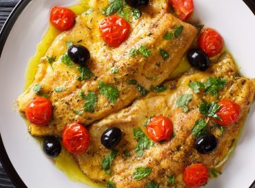 Spicy trout fillet with garlic lemon butter sauce, tomatoes and olives close-up on a plate. Horizontal top view
