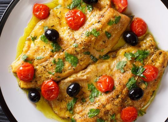 Spicy trout fillet with garlic lemon butter sauce, tomatoes and olives close-up on a plate. Horizontal top view