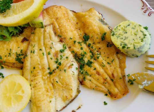 fried plaice fillet with herb butter and lemon on a plate, typical food in northern germany at the coast, high angle view, above