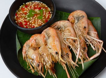 grilled prawns with spicy dipping sauce on banana leaf in black disk on white background
