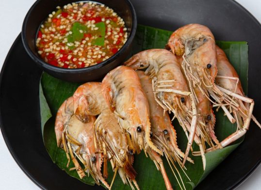 grilled prawns with spicy dipping sauce on banana leaf in black disk on white background