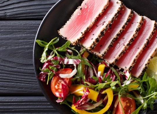 Close up of rare seared Ahi tuna slices with fresh vegetable salad. Top view horizontal