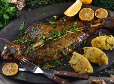 Two whole fresh flounder, butter, and lemon on black baking sheet  Sole Meuniere recipe