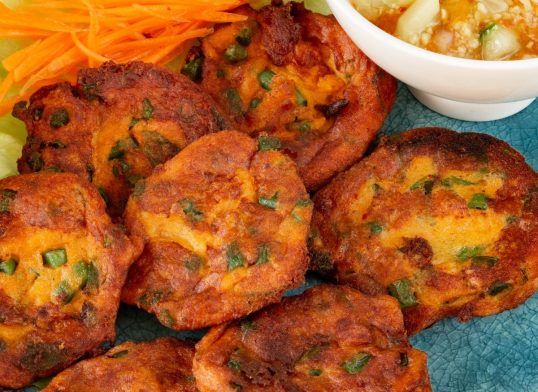 Homemade Thai fish cakes with cucumber dipping sauce and salad on a turquoise plate