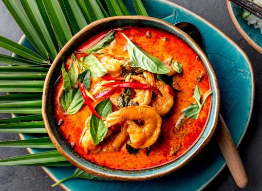 THAI SHRIMPS RED CURRY. Thailand Thai tradition red curry soup with shrimps prawns and coconut milk. Panaeng Curry in blue plate on gray background