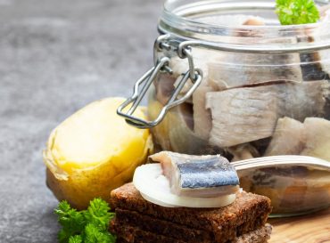 Homemade marinated herring in glass jar with rye bread and jacket potato on gray table