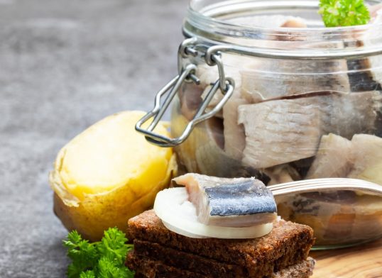 Homemade marinated herring in glass jar with rye bread and jacket potato on gray table
