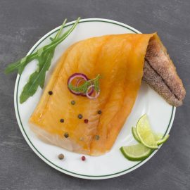 beautiful yellow smoked haddock fish fillet on a plate with a branch of fresh arugula, lime and pink berry on grey slate background